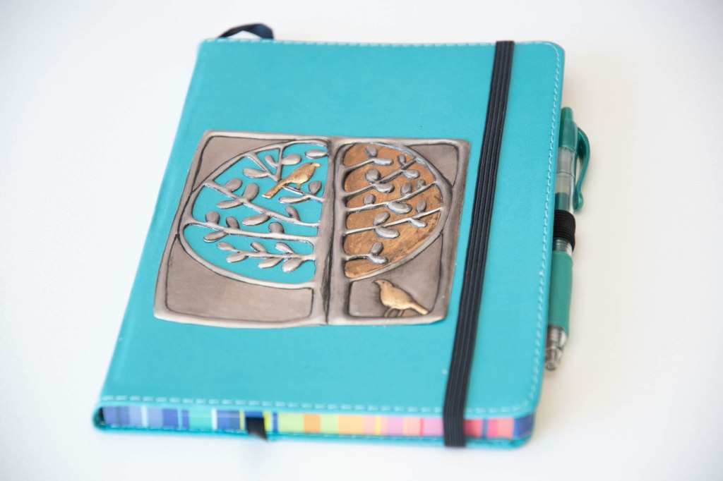 An embossed pewter design of two birds in a tree on a journal by artist Sandy Griffiths.