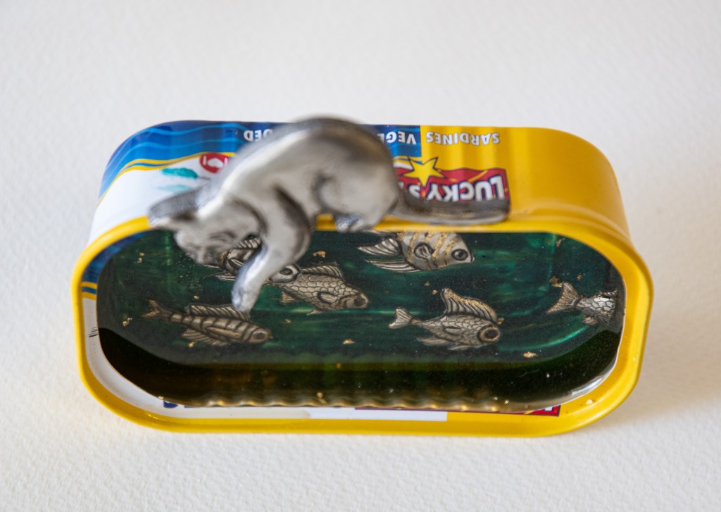 Pewter art by Sandy Griffiths entitled Lucky cat. Embossed Pewter cat looking at fish set in resin in a Lucky Fish Sardine tin. 80 x 105mm
