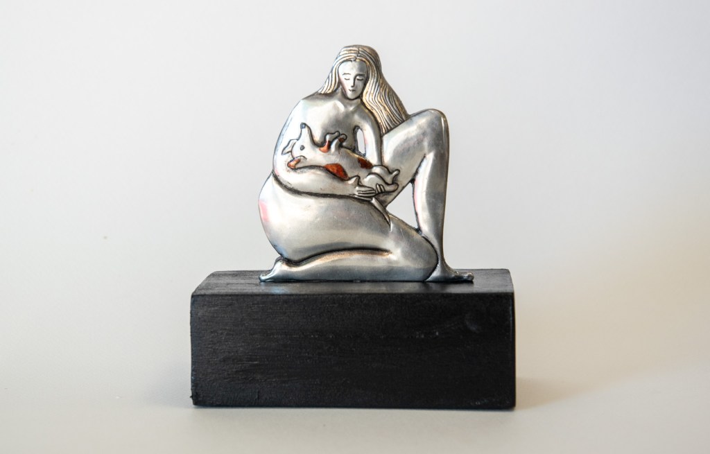 A pewter artwork showing a Lady with a dog and cat (front view). Embossed pewter on a wooden plinth. 160 x 140 x 70mm.
