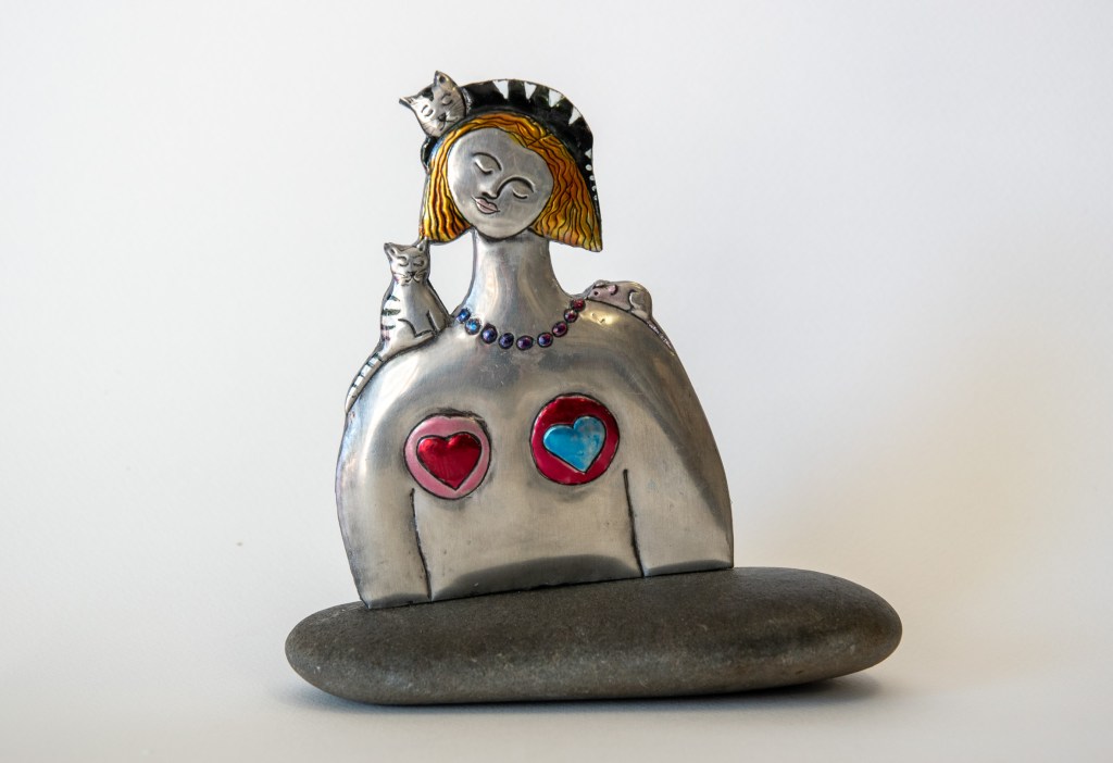 Embossed pewter artwork showing a Red Head Lady with a cat on her shoulder. Embossed pewter on a river stone by pewter artist Sandy Griffiths. 170 x 180 x 70mm.