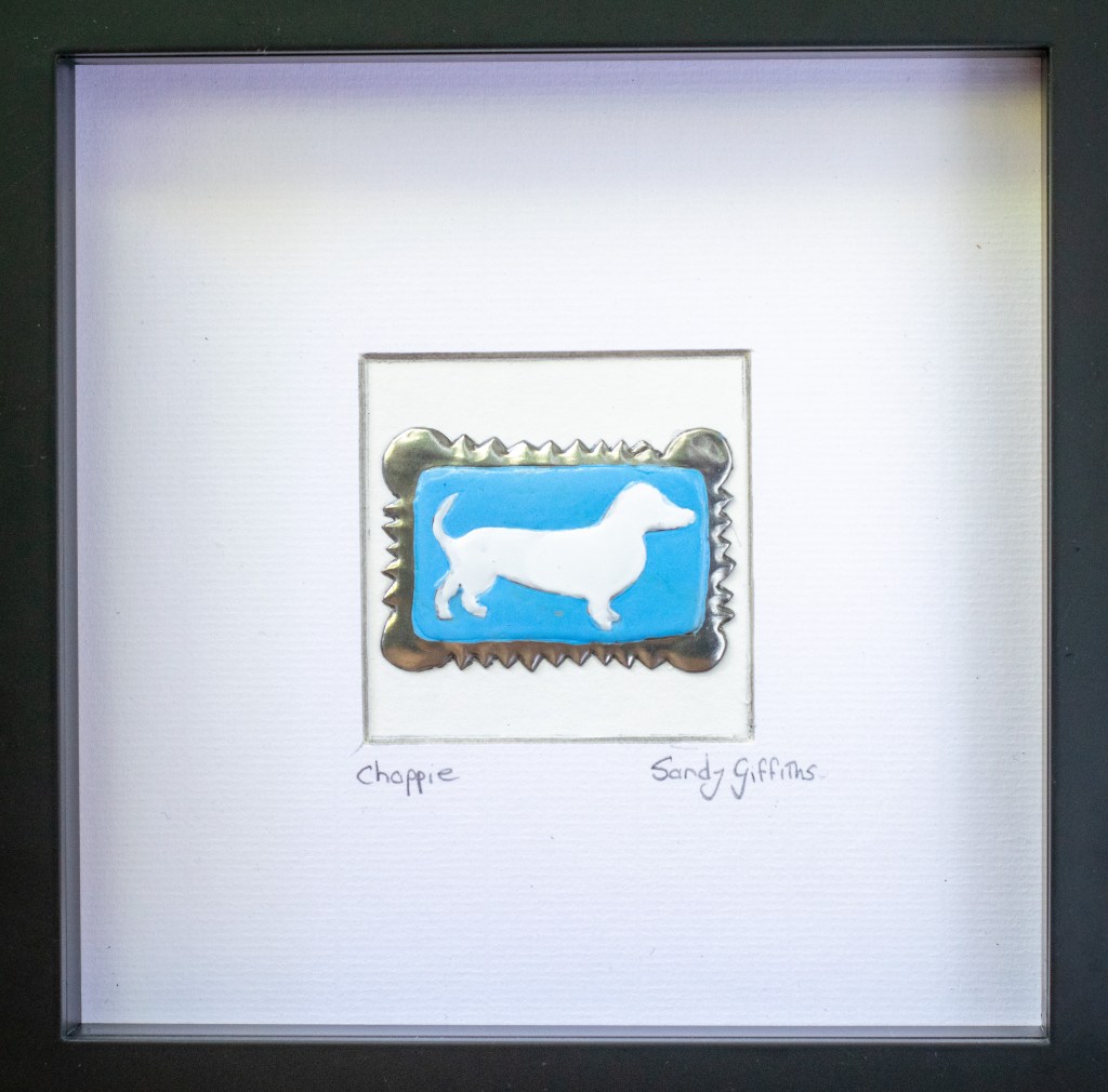 A Sausage Dog Zoo biscuit made from Embossed Pewter and paint in black box frame by Pewter artist sandy Griffiths. 190mm x 190mm. R950.00