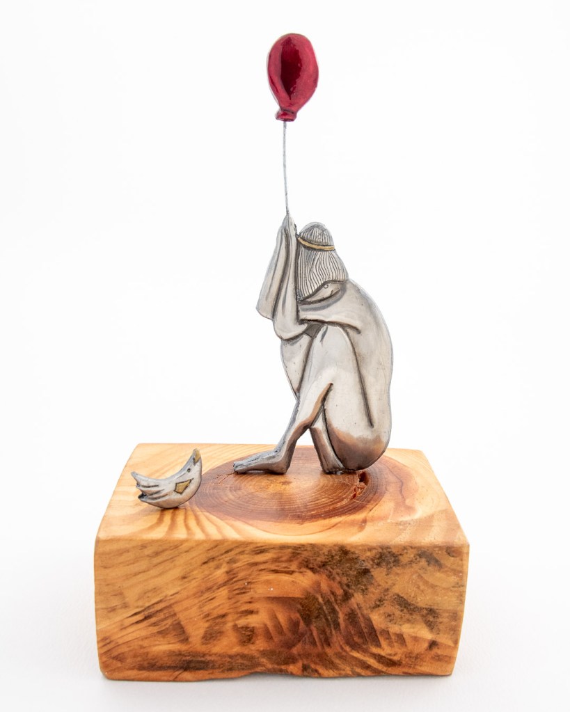 Hand-embossed pewter girl holding a balloon and a bird set on clay, mounted on a piece of knotty Pine, by Sandy Griffiths. 140 x 100 x 230mm.