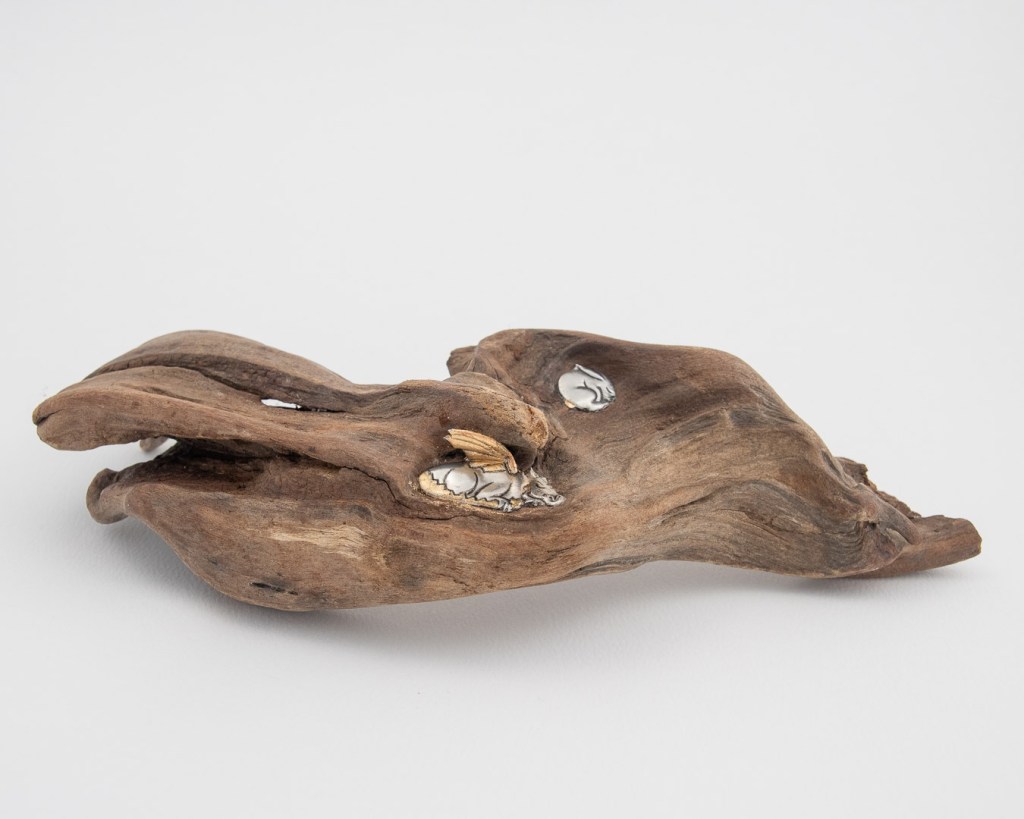 Hand-embossed pewter rabbit and dragon sculpture asleep in the hollow of a piece of driftwood found at a river by Sandy Griffiths. 270 x 110 x 60mm.