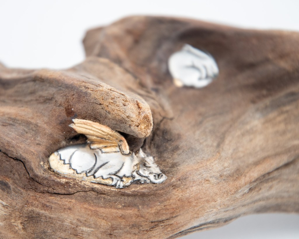 Hand-embossed pewter rabbit and dragon sculpture asleep in the hollow of a piece of driftwood found at a river by Sandy Griffiths. 270 x 110 x 60mm.